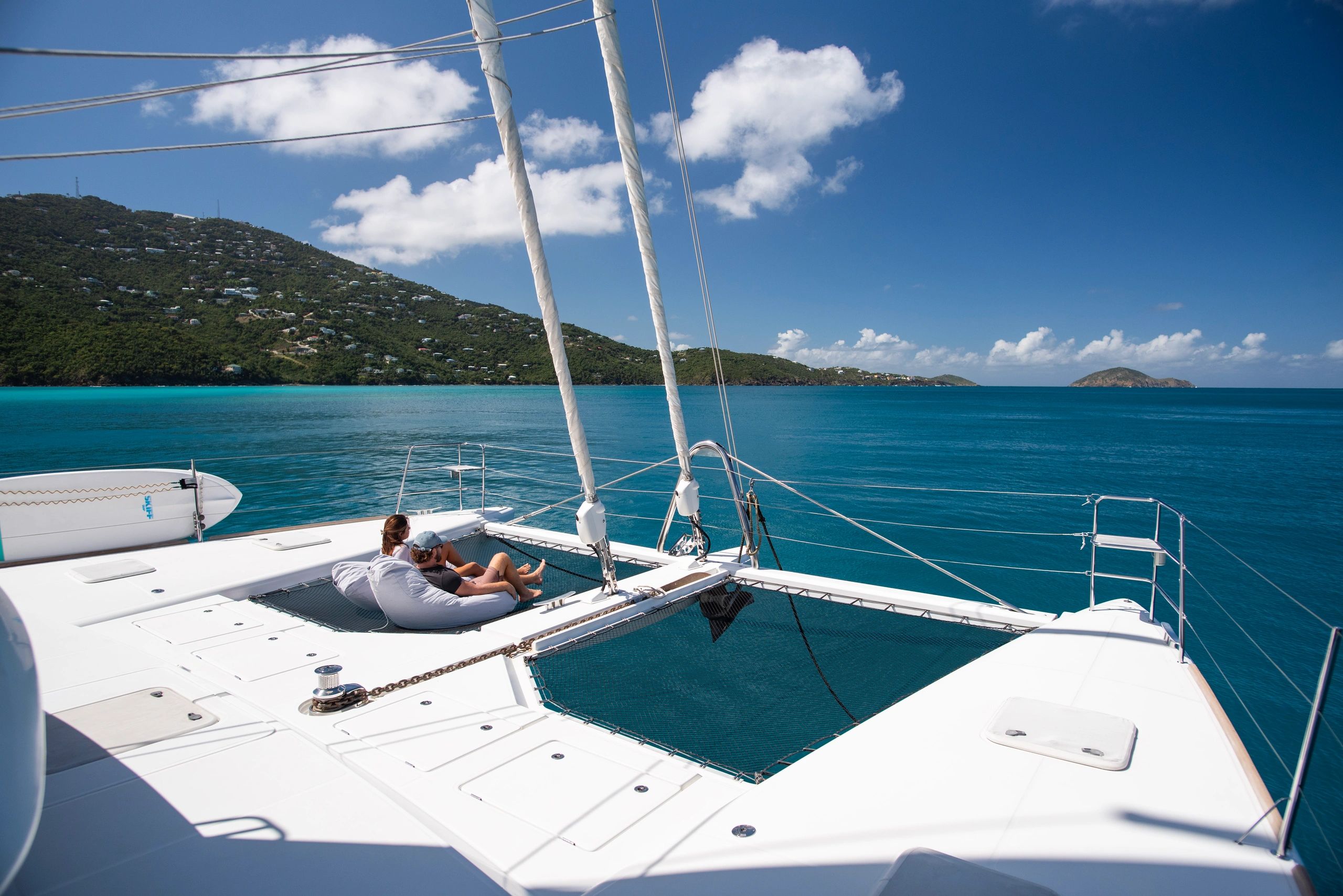 Guests relaxing on Ripple catamaran trampoline in turquoise Caribbean waters