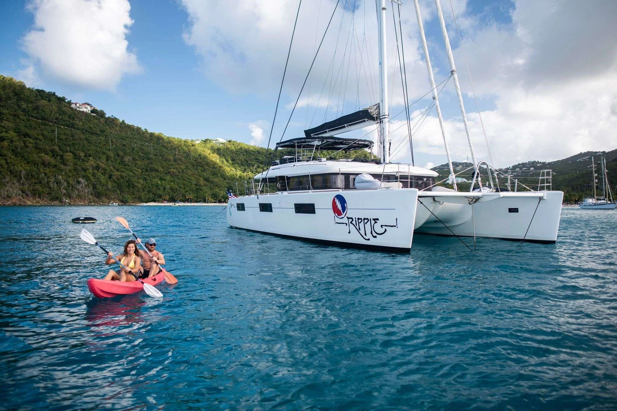 Ripple catamaran anchored near tropical coastline with guests kayaking