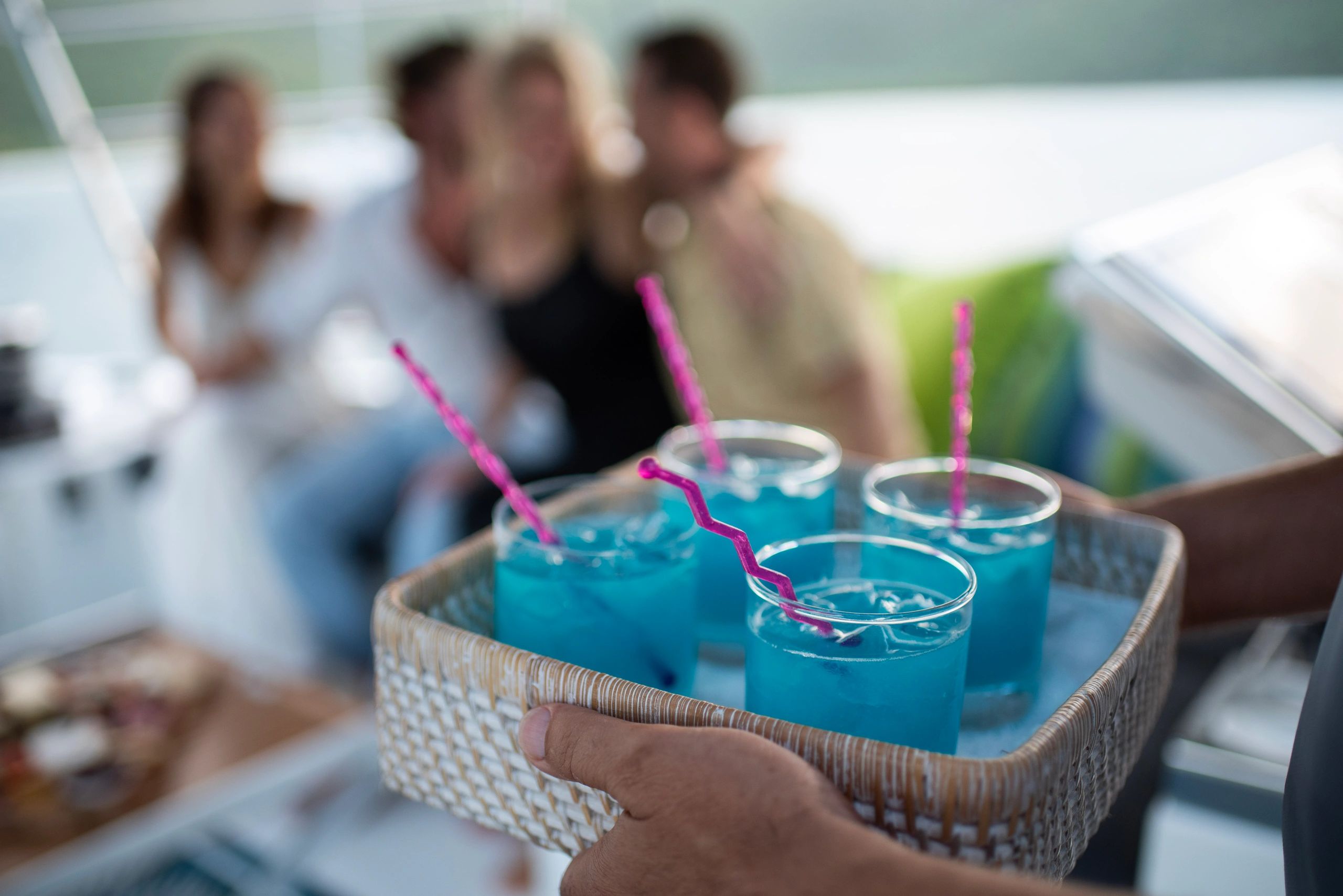 Turquoise cocktails served on a woven tray with guests socializing aboard